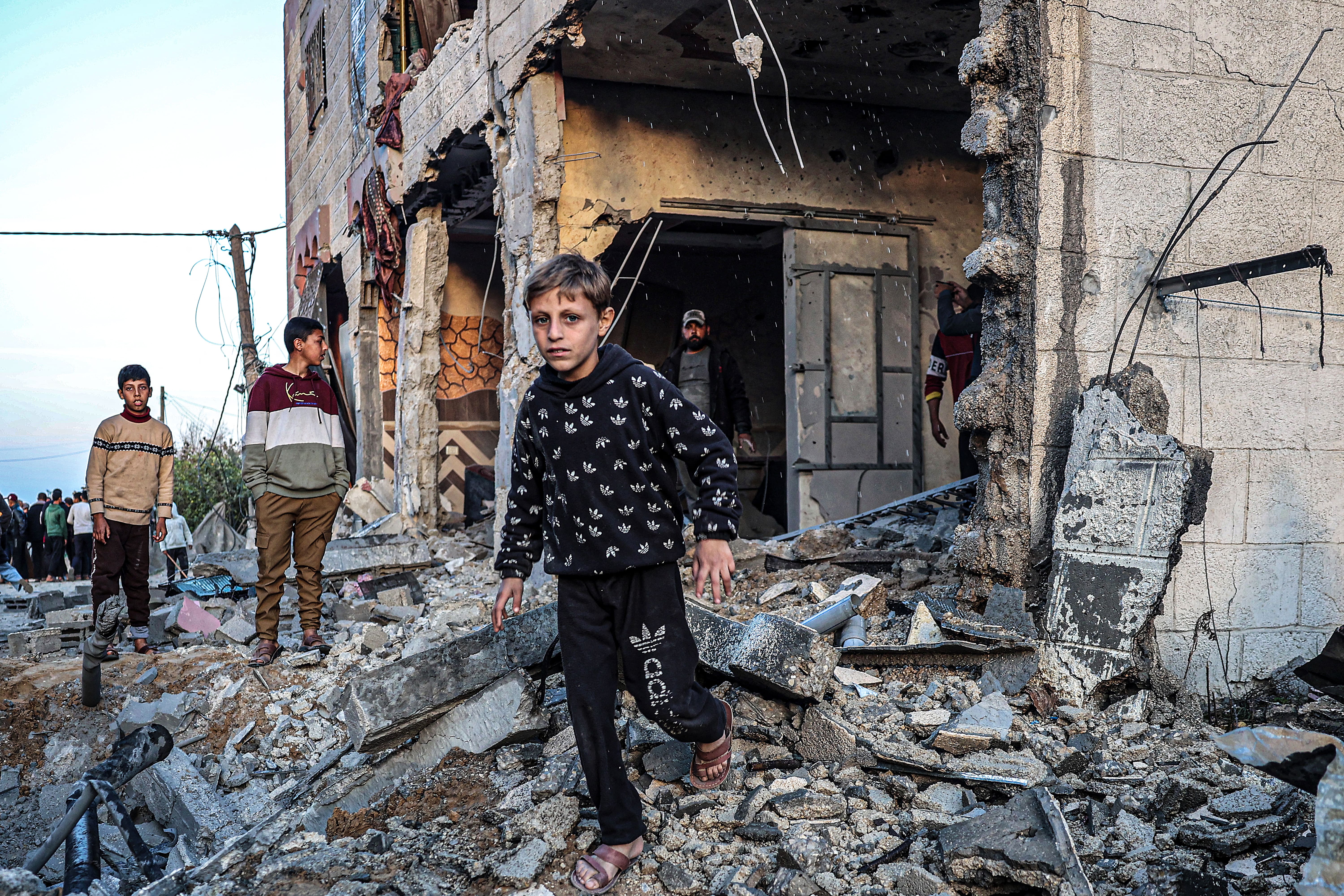 Orang-orang berjalan melewati puing-puing bangunan yang rusak berat akibat bom dari Israel di Rafah, Jalur Gaza, Palestina pada Minggu (11/2/2024). (Foto: AFP/Said Khatib)
