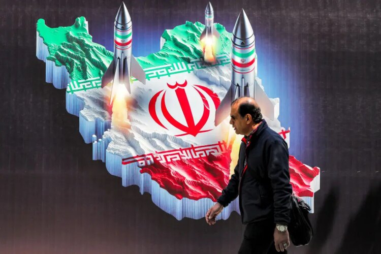 Seorang pria berjalan melewati spanduk bergambar peluncuran rudal dari representasi peta Iran yang diwarnai dengan bendera Iran di pusat kota Teheran, Senin (15/4/2024). (Foto: AFP/Atta Kenare)