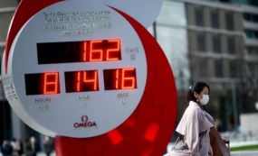 Seorang warga Jepang menggunakan masker melewati jam countdown digital Olimpiade 2020 di Tokyo, Senin (16/3/2020. (ANTARA/REUTERS/Edgard Garrido)